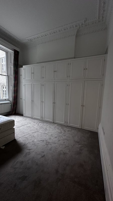 A bedroom with painted fitted cupboards and ornate cornicing.