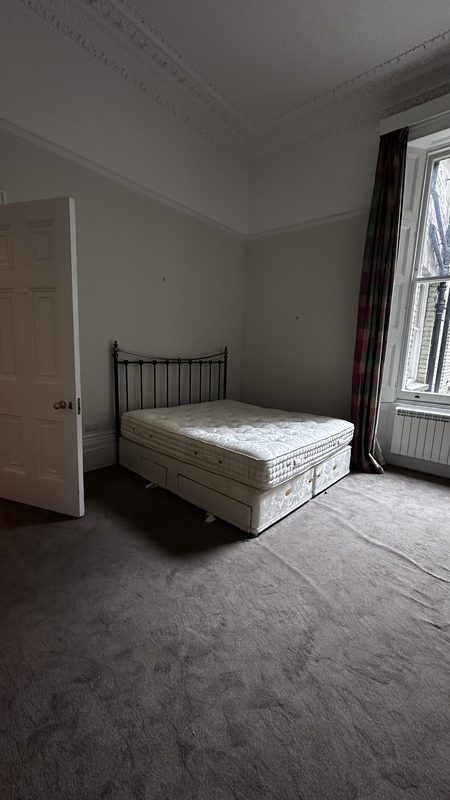 A bedroom before the work, an iron bed under a tall window.