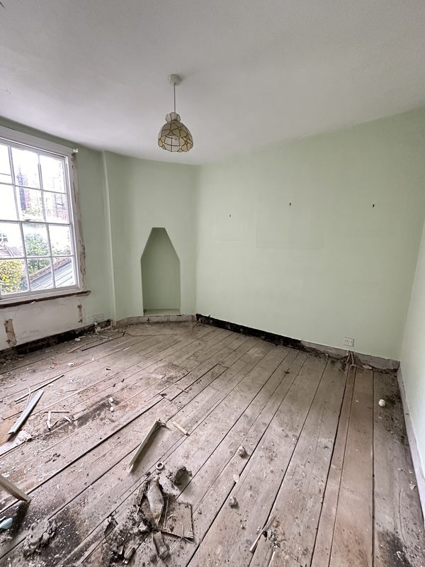 A green painted bedroom with bare boards, before the work.