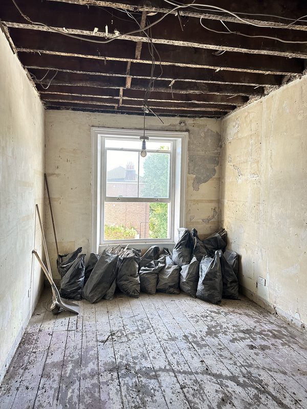 A front room stripped to the boards, rubble bags under the window.