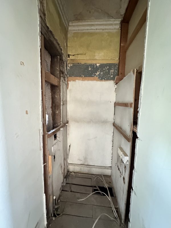 A narrow room stripped back to plaster and lath.