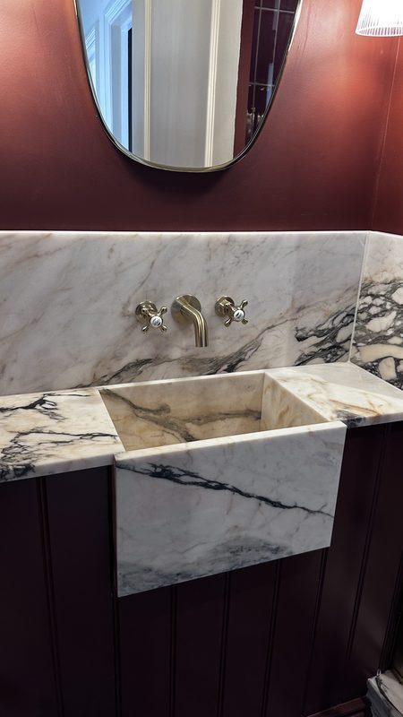 A Calacatta Viola marble basin with brass taps against an oxblood wall.