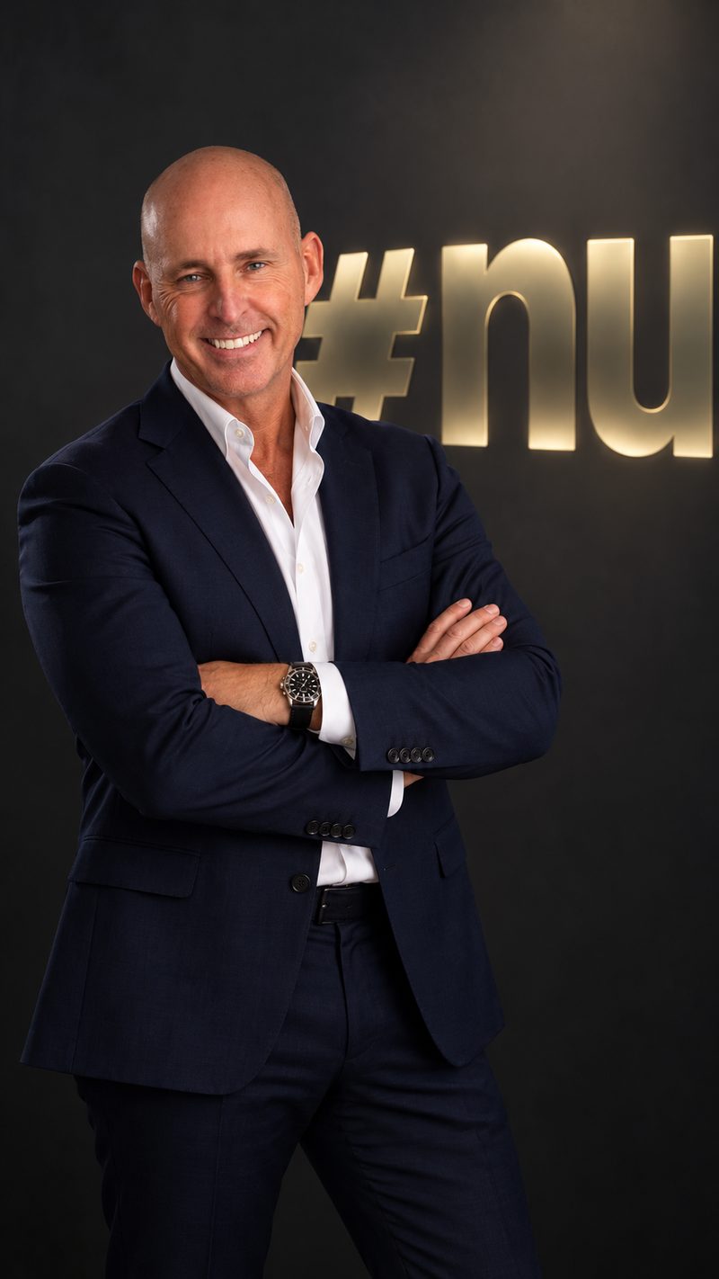 Nick Jeffries, founder of NU Projects, smiling with his arms crossed, in a navy suit beside the gold #nu sign