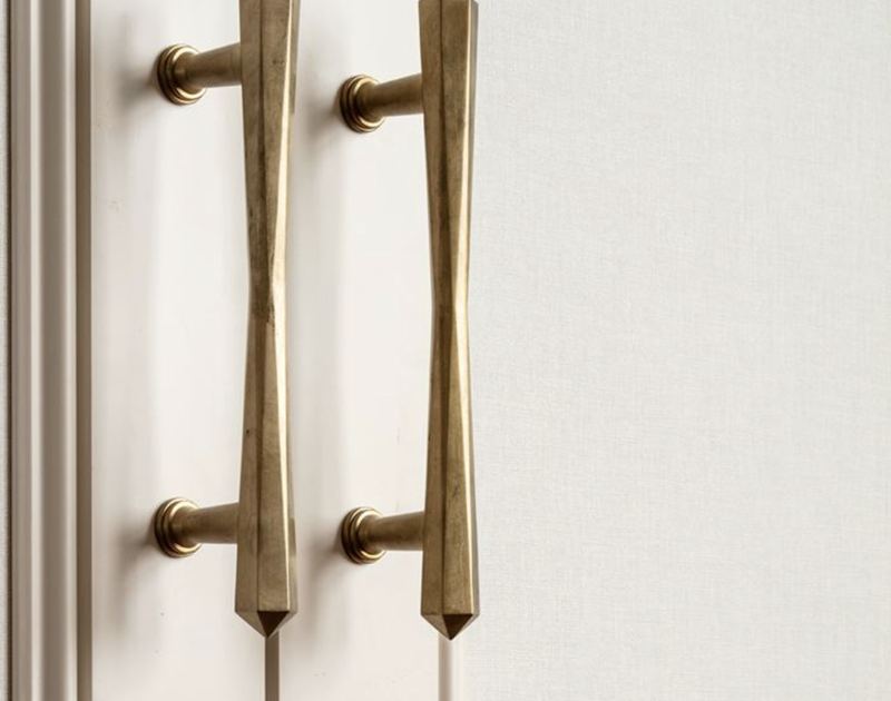 A pair of faceted bronze pull handles on a pale painted door.