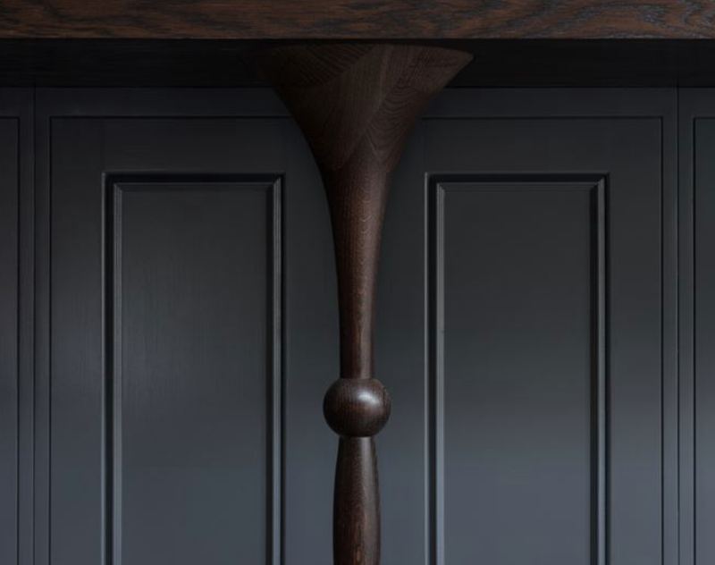 Turned dark oak leg beneath an island, set against painted panelled doors.