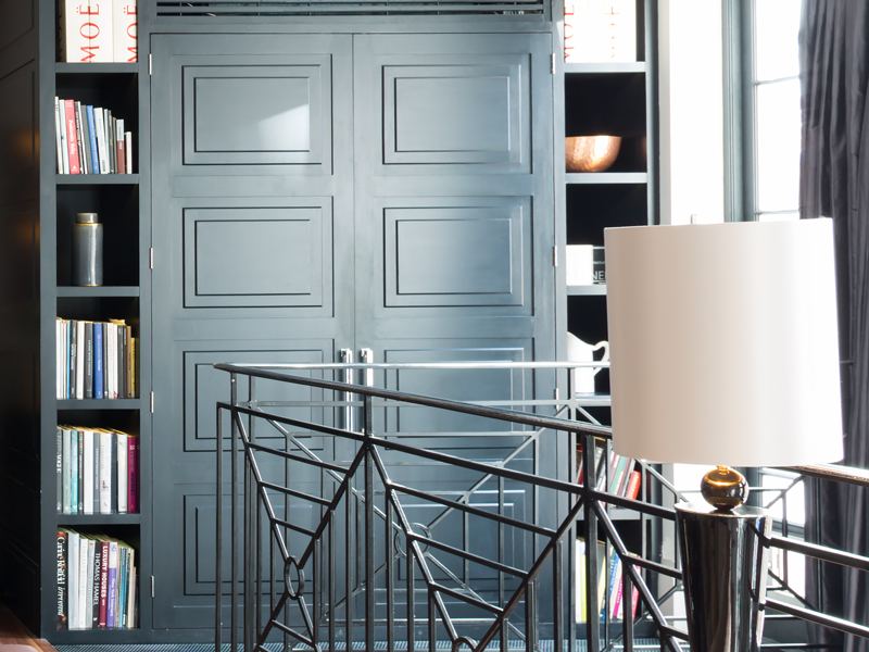 Floor to ceiling bookshelves either side of tall panelled doors in a grey painted room.