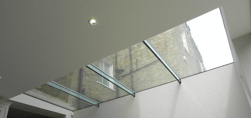 Looking up through a frameless structural glass roof with glass fins to the brick rear wall of the neighbouring house.