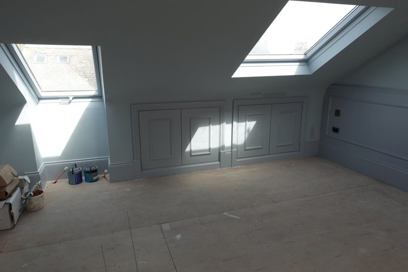 London loft room mid works. Two rooflights, painted panelled eaves cupboards, a ply floor and first fix sockets on the wall before decoration.