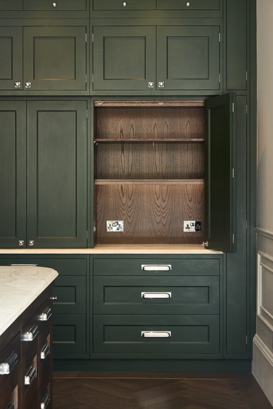 Green larder opened to show timber lined shelves and sockets.