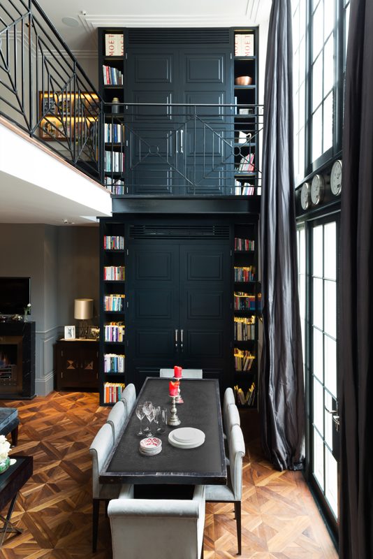 Double height room lined with bookshelves and steel framed glazing.
