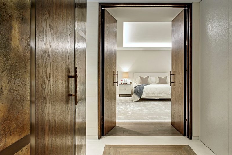 Bronze panelled doors opening onto a pale principal bedroom.