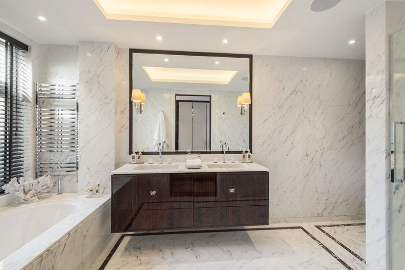 Bathroom with a dark vanity and book matched marble walls.