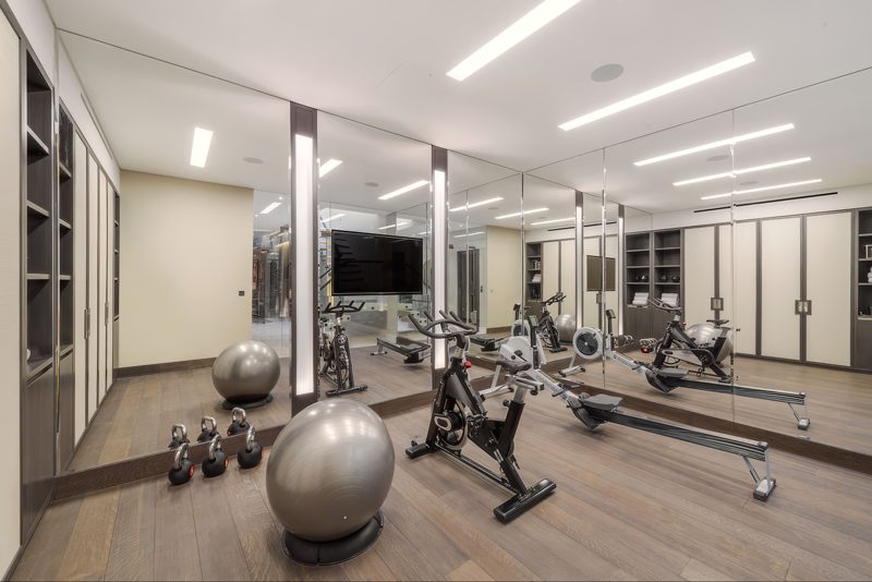 Basement gym with mirrored walls between lit pilasters, a spin bike and a rowing machine.