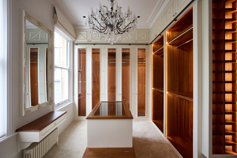 Dressing room lined in walnut with a chandelier and island.