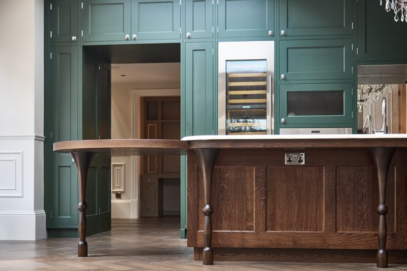 Green painted kitchen with a dark oak island on turned legs.