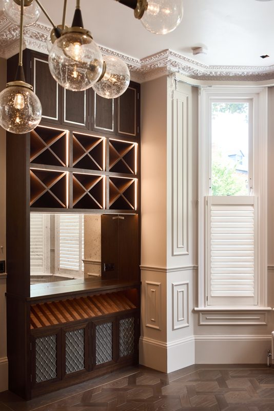 Dark timber wine rack and cabinets beside a shuttered bay window.