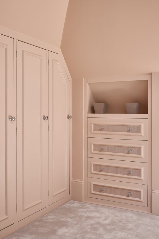 Fitted wardrobes and drawers painted blush pink under the eaves.