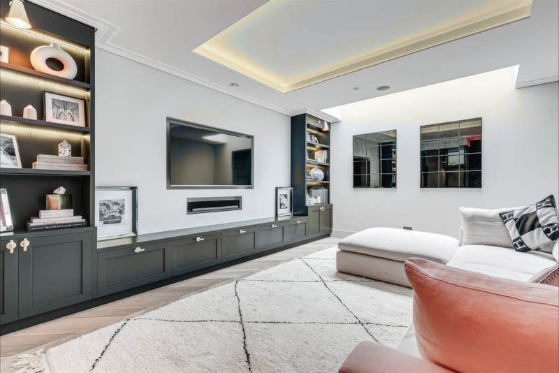 Basement media room with dark joinery, a long fire and warm cove lighting.