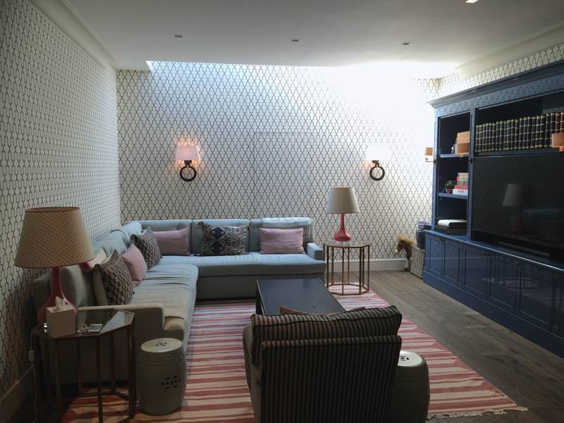 Basement family room under a light well, with painted joinery and patterned walls.