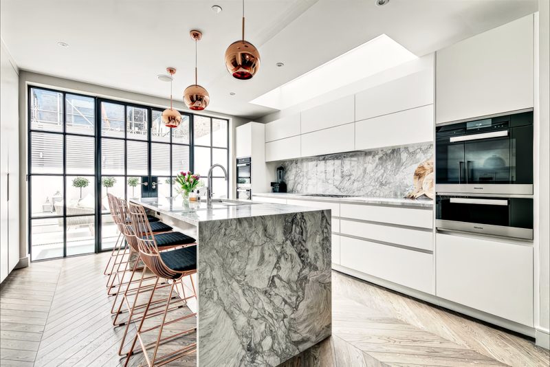 Kitchen with a marble waterfall island, steel-framed glazing and a long rooflight.