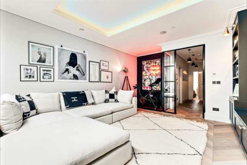 Living room with a deep sofa, warm cove lighting and a glazed door to the hall.