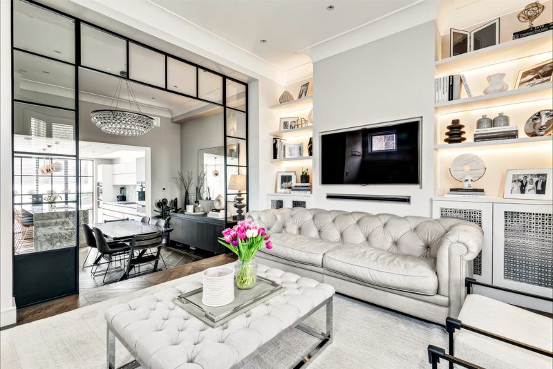 Reception room with a tufted sofa and lit shelving, behind a steel-framed screen.