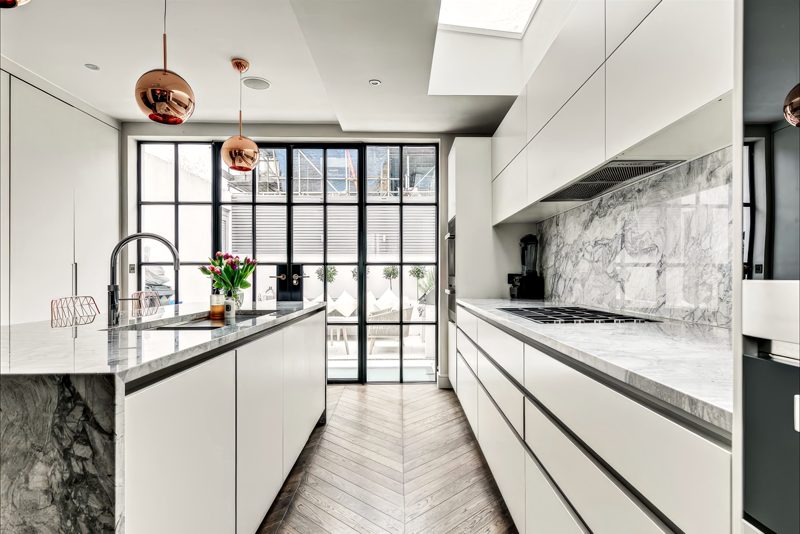 Galley of handleless units and marble worktops below a rooflight.