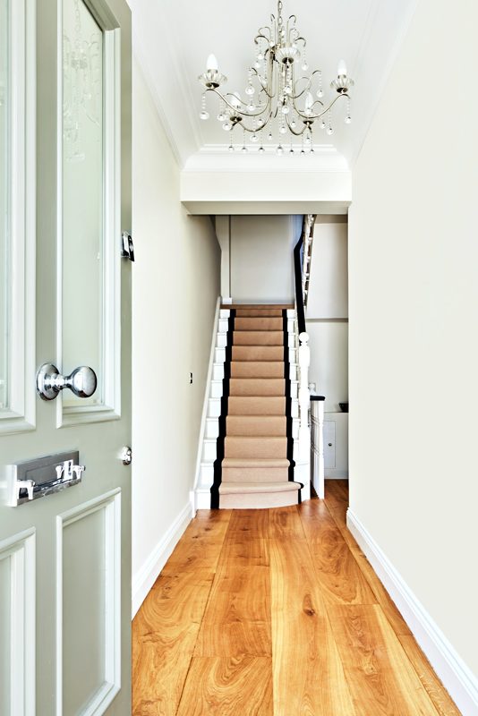 Hall with a tall door, oak boards and the stair rising beyond.