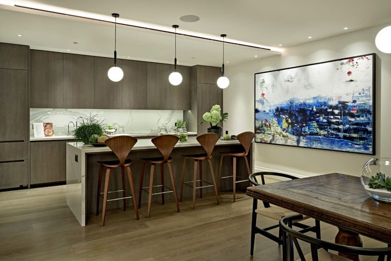 Kitchen with dark timber units, pale stone worktops and walnut bar stools.