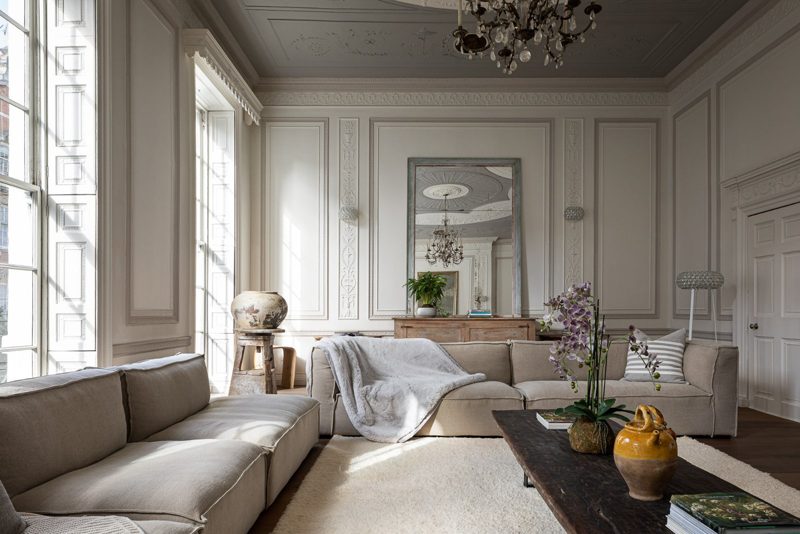 Drawing room with low sofas beside a tall sash window and panelled walls.