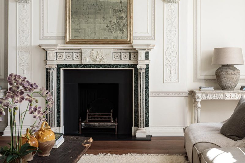 Detail of a carved marble chimneypiece with a dark stone surround.