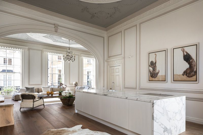 Marble kitchen island under an ornate ceiling, with the arch to the drawing room beyond.