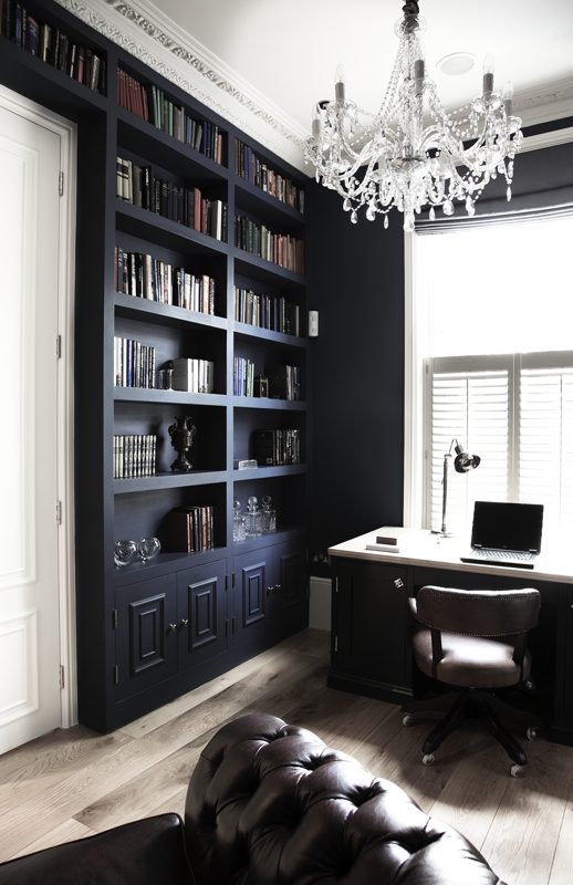 Study with navy bookshelves, a chandelier and a leather chair.