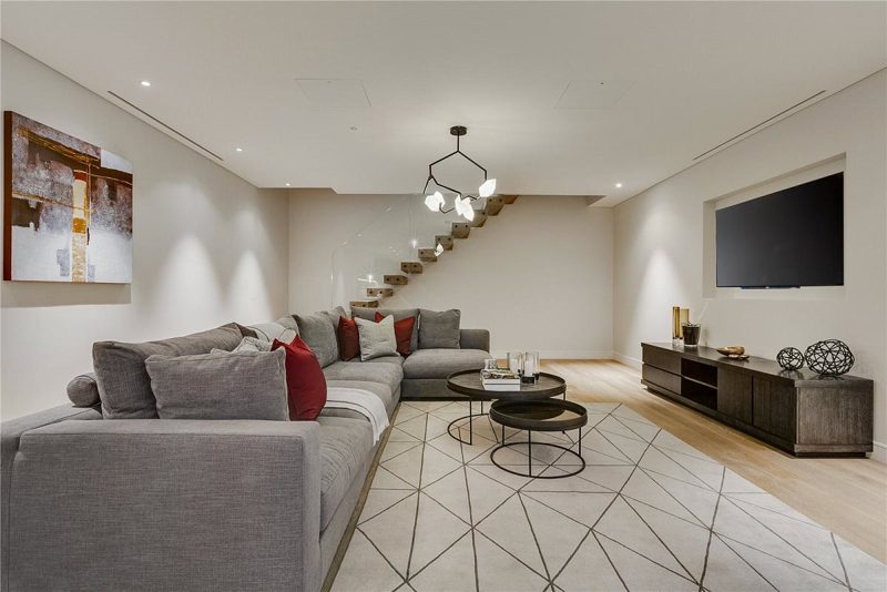 Family room with a grey corner sofa below a floating stair.