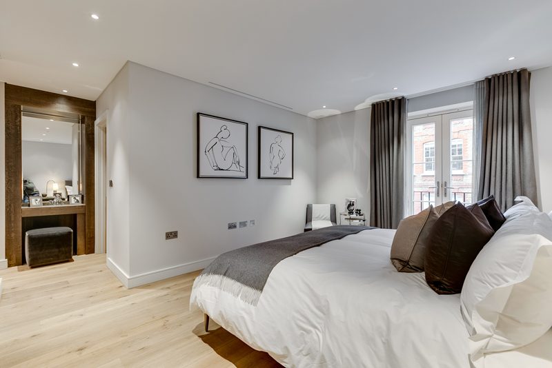 Bedroom with oak floors, a dressing table and French windows.