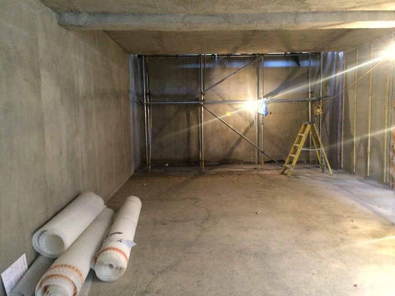 A cast concrete basement floor, empty, with rolls of membrane and site lights.