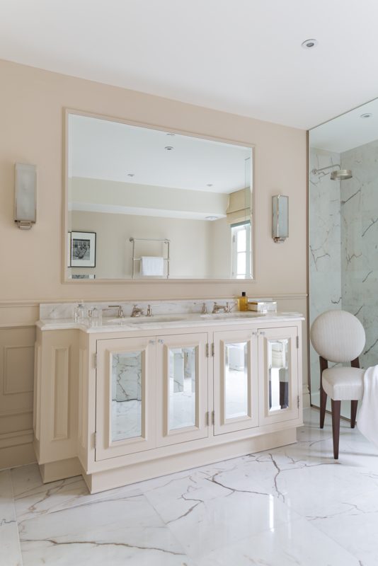 Bathroom with a pale vanity, marble top and wide mirror.