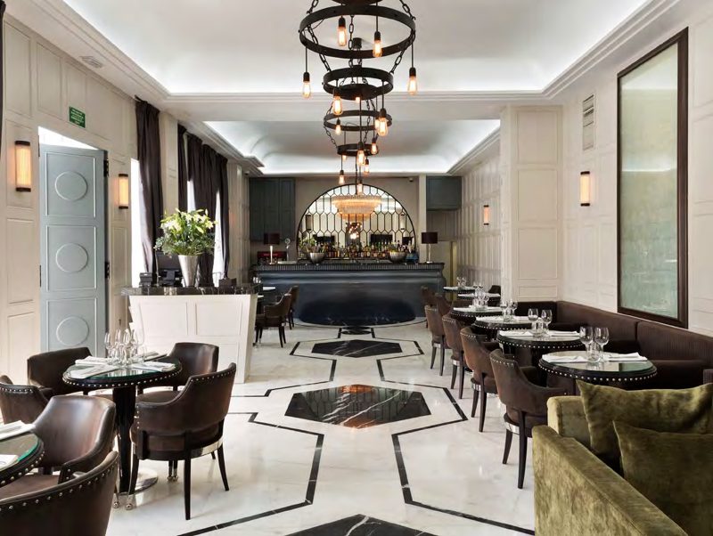A hotel lounge and bar with a black and white marble floor, a tiered iron chandelier and panelled walls.