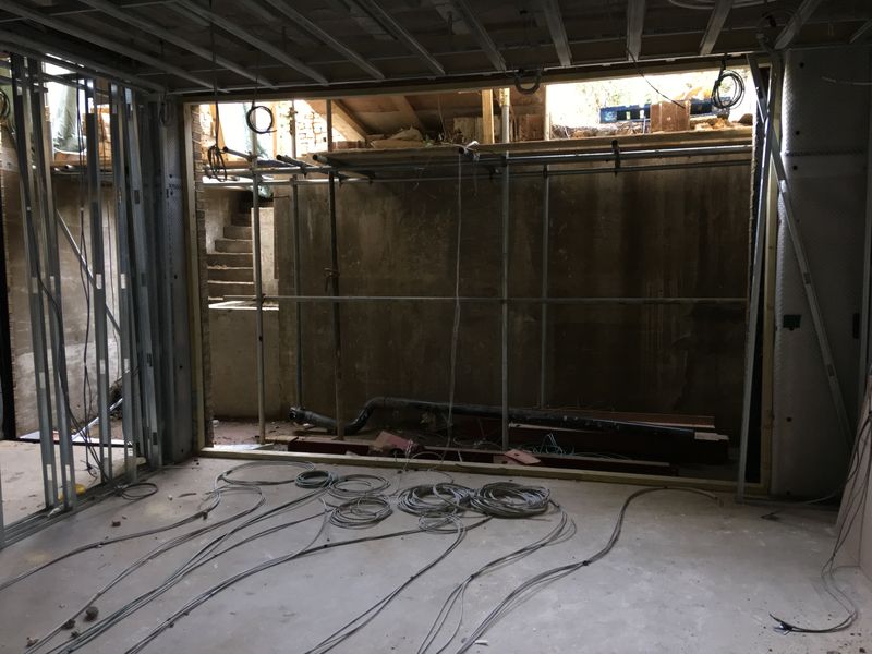 A lower ground floor opened up, with cables coiled on the slab, steel stud framing at the side and a drainage pipe on the floor.